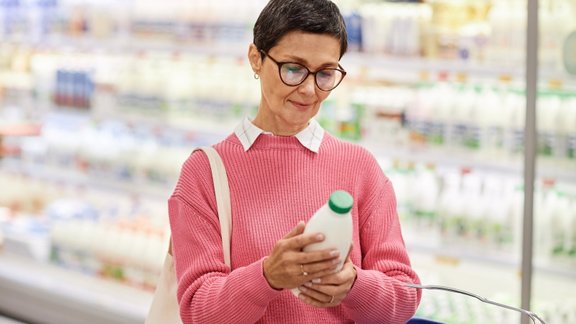 basket,mature,aisle,freshness,housewife,shopping,smiling,mall,milk,dairy product,cheerful,healthy eating,lifestyles,buyer,quality,market,nutrition,freezer,senor,adult,groceries,pink,shop,woman,color,expiration date,bottle,choosing,retail,convenience store