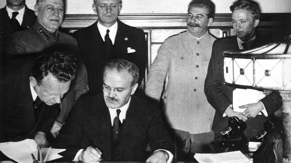 Soviet_Foreign_Minister_Molotov_signs_the_German-Soviet_non-aggression_pact,_Joachim_von_Ribbentrop_and_Josef_Stalin_sta_-_NARA_-_540196