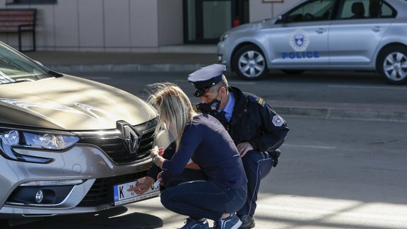 Kosovas policists palīdz serbu autovadītājai pielikt speciālu uzlīmi.